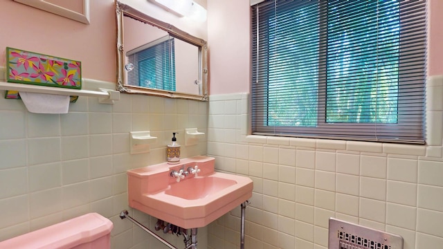 bathroom with a wainscoted wall, a sink, tile walls, and toilet