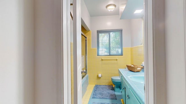 bathroom featuring toilet, tile walls, vanity, wainscoting, and tile patterned floors