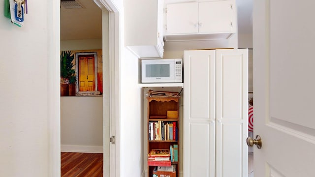 hall with wood finished floors, visible vents, and baseboards