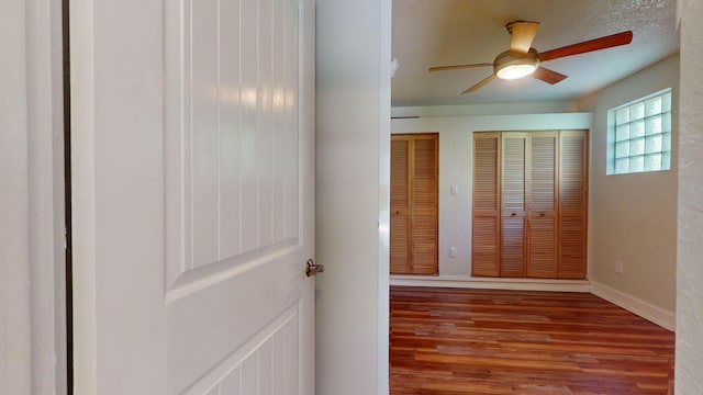 unfurnished bedroom with ceiling fan, multiple closets, wood finished floors, and baseboards