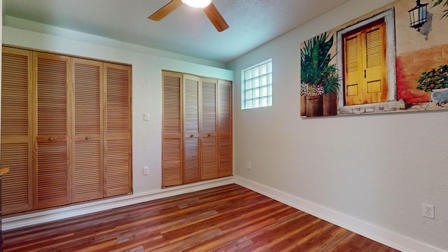 unfurnished bedroom with ceiling fan, two closets, baseboards, and wood finished floors