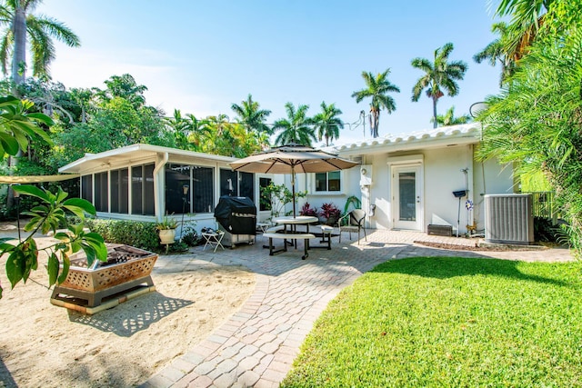 back of property featuring a patio, stucco siding, central air condition unit, a lawn, and a sunroom