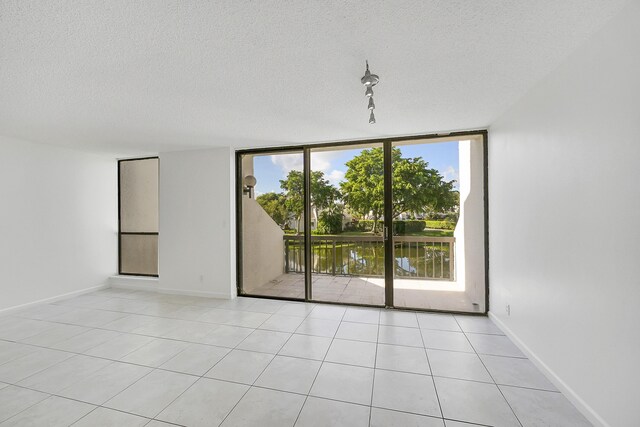 empty room featuring floor to ceiling windows, track lighting, light tile patterned flooring, a textured ceiling, and a water view