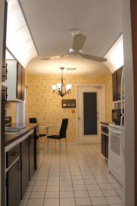 kitchen with light tile patterned flooring, ceiling fan with notable chandelier, white electric range, sink, and hanging light fixtures