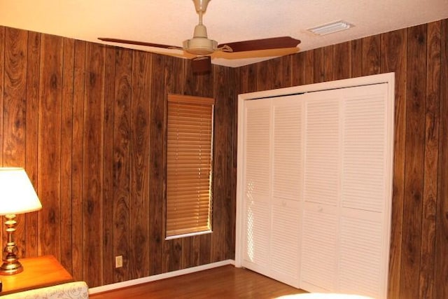 unfurnished bedroom with dark wood-type flooring, a closet, ceiling fan, and wood walls