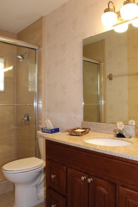 bathroom featuring tile patterned flooring, toilet, vanity, and a shower with shower door