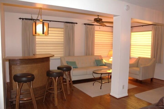 living room with hardwood / wood-style flooring, ceiling fan, and bar area