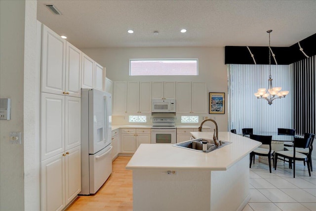 kitchen with sink, an island with sink, pendant lighting, white appliances, and white cabinets