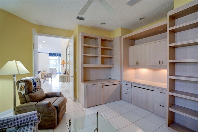 interior space with light tile patterned flooring, ceiling fan, a textured ceiling, and light brown cabinetry