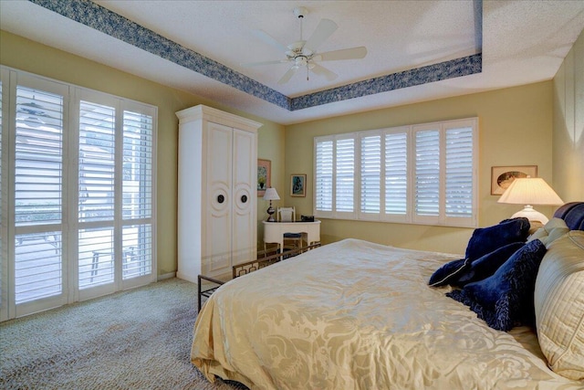 carpeted bedroom featuring ceiling fan, a tray ceiling, multiple windows, and a textured ceiling