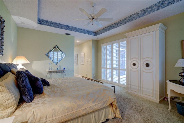 carpeted bedroom with ceiling fan and a tray ceiling