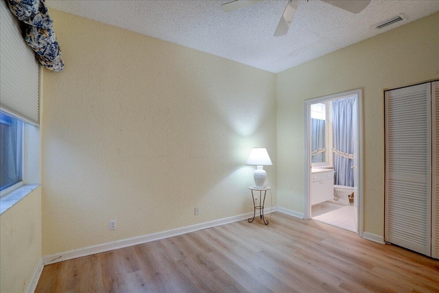 unfurnished bedroom featuring ceiling fan, ensuite bath, light hardwood / wood-style floors, and a textured ceiling