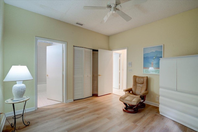 living area featuring ceiling fan, light hardwood / wood-style floors, and a textured ceiling