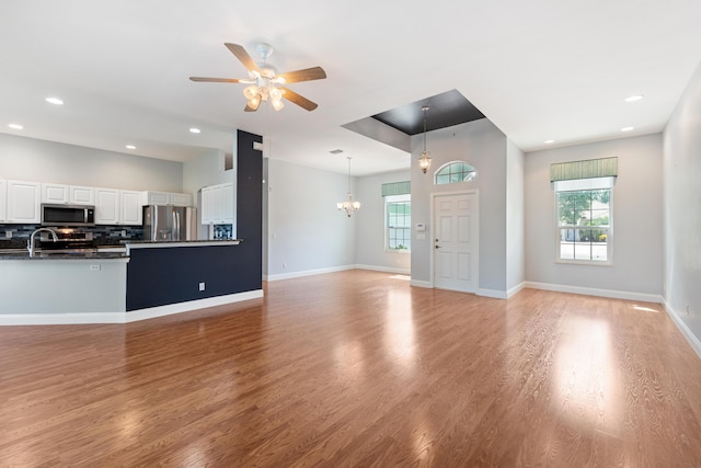 unfurnished living room with a healthy amount of sunlight, ceiling fan with notable chandelier, and light hardwood / wood-style flooring