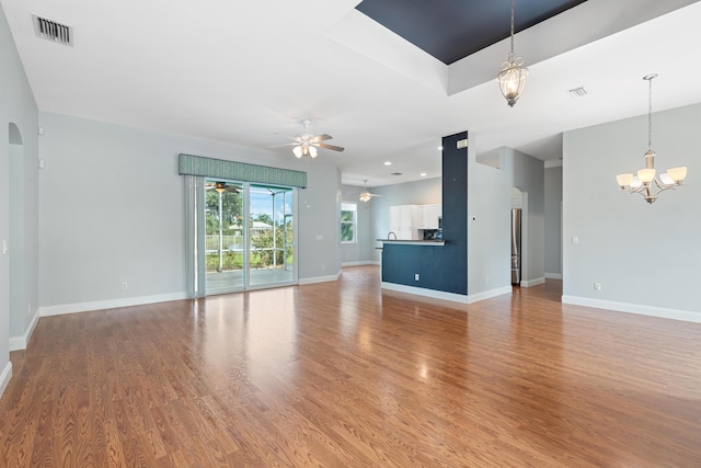 unfurnished living room with ceiling fan with notable chandelier and light hardwood / wood-style flooring