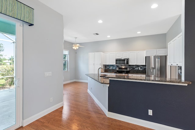 kitchen featuring appliances with stainless steel finishes, white cabinetry, dark stone countertops, backsplash, and kitchen peninsula