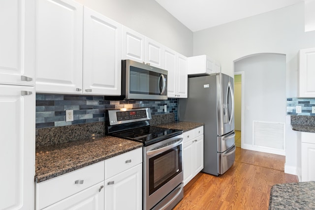 kitchen featuring white cabinetry, stainless steel appliances, tasteful backsplash, dark stone countertops, and light wood-type flooring