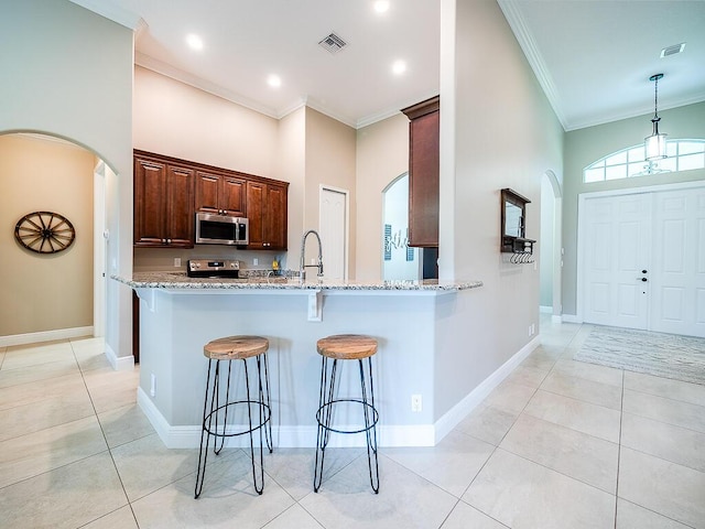 kitchen featuring light tile patterned flooring, kitchen peninsula, stainless steel appliances, crown molding, and light stone countertops