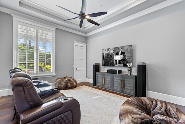 living room with a raised ceiling, ornamental molding, hardwood / wood-style flooring, and ceiling fan