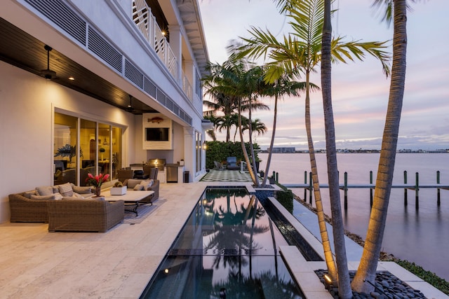 pool at dusk featuring a water view, area for grilling, an outdoor living space, and a patio area