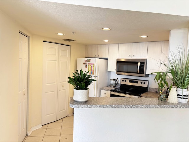 kitchen with kitchen peninsula, light tile patterned floors, appliances with stainless steel finishes, and a textured ceiling