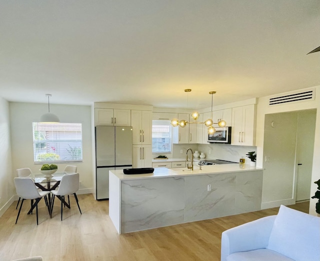 kitchen featuring light wood-type flooring, stainless steel appliances, white cabinetry, and hanging light fixtures