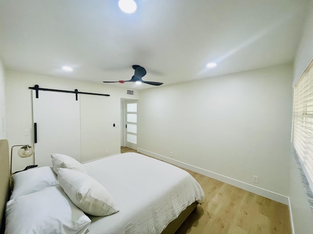 bedroom featuring ceiling fan, a barn door, and light hardwood / wood-style flooring