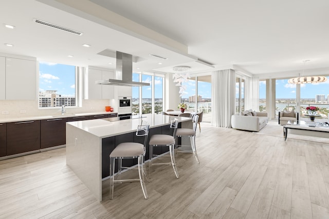 kitchen with a breakfast bar, white cabinetry, island range hood, dark brown cabinets, and a kitchen island