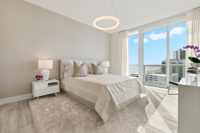 bedroom featuring a water view, expansive windows, and light wood-type flooring