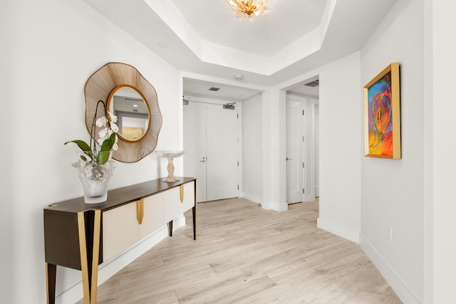 corridor with a tray ceiling and light hardwood / wood-style flooring