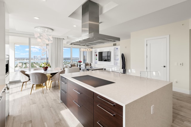 kitchen with a large island, dark brown cabinetry, black electric stovetop, island range hood, and light wood-type flooring