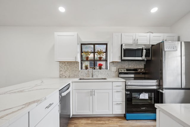 kitchen featuring sink, light hardwood / wood-style flooring, appliances with stainless steel finishes, white cabinetry, and backsplash