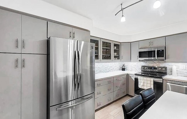 kitchen featuring glass insert cabinets, gray cabinets, backsplash, and stainless steel appliances
