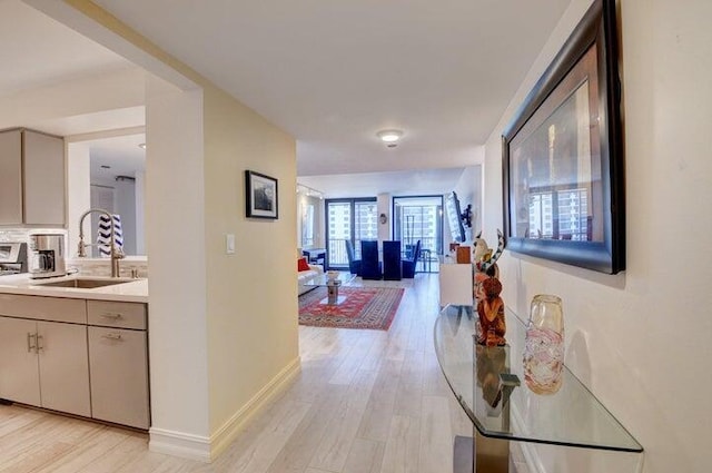 corridor featuring baseboards, a sink, and light wood-style flooring