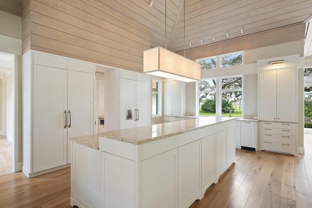 kitchen featuring white cabinetry, wooden walls, a towering ceiling, light stone counters, and a center island