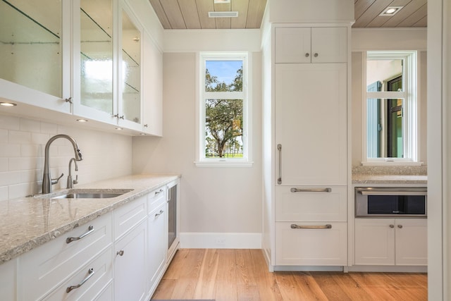 kitchen featuring tasteful backsplash, sink, white cabinetry, light wood-type flooring, and light stone counters