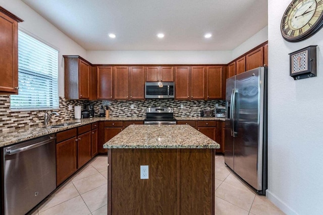 kitchen featuring light stone counters, sink, appliances with stainless steel finishes, and a center island