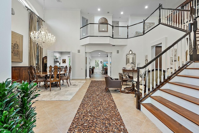 tiled foyer featuring crown molding, a high ceiling, and a chandelier