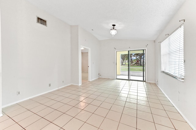 empty room featuring vaulted ceiling, light tile patterned flooring, and a textured ceiling