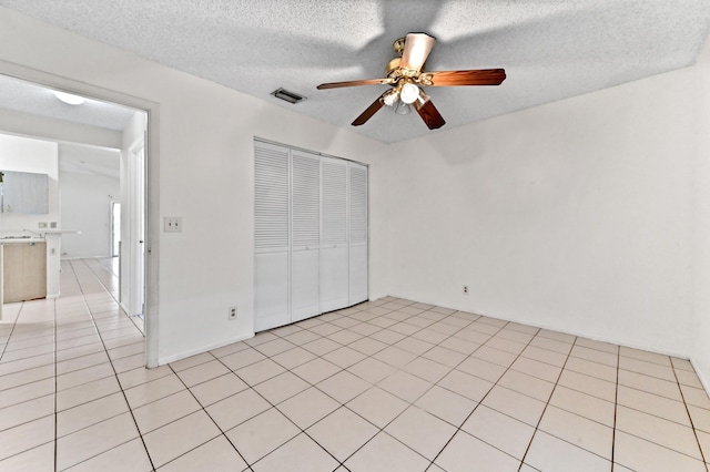 unfurnished bedroom with ceiling fan, a textured ceiling, a closet, and light tile patterned floors