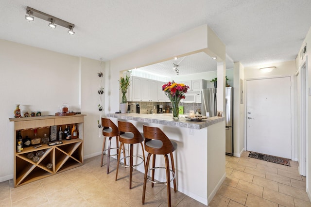 kitchen with white cabinetry, a kitchen bar, kitchen peninsula, stainless steel fridge, and decorative backsplash