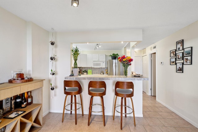 kitchen featuring a breakfast bar, kitchen peninsula, stainless steel fridge, and white cabinetry