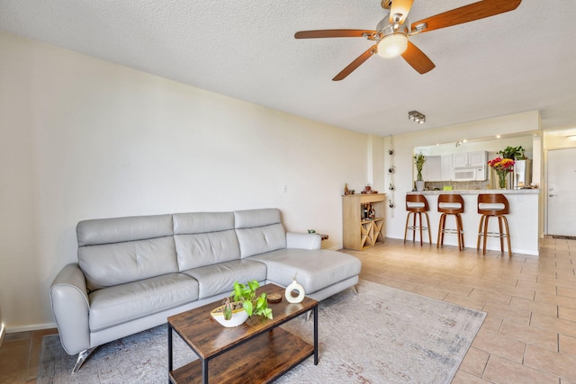 living room featuring ceiling fan, light tile patterned floors, and a textured ceiling