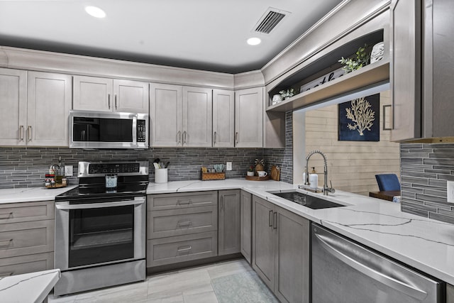 kitchen featuring light stone countertops, stainless steel appliances, sink, backsplash, and gray cabinets