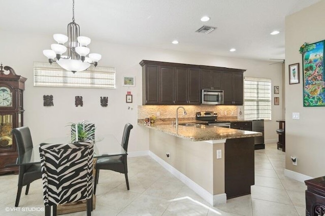 kitchen with appliances with stainless steel finishes, decorative light fixtures, sink, kitchen peninsula, and light stone counters