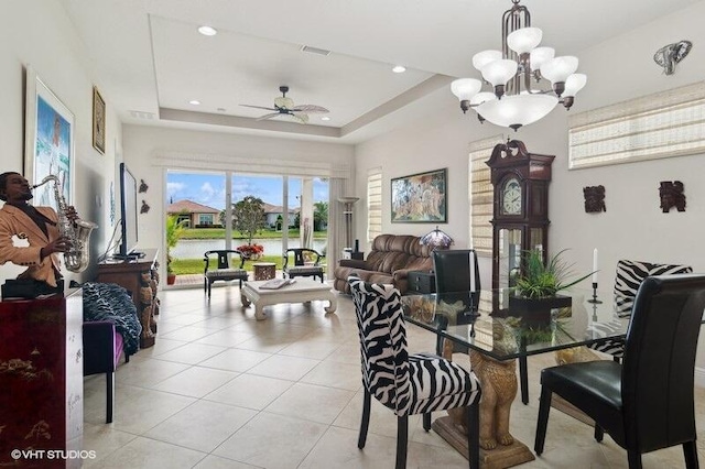 tiled dining area with ceiling fan with notable chandelier and a tray ceiling