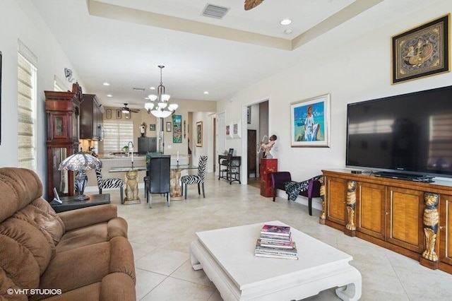 tiled living room with ceiling fan with notable chandelier and a raised ceiling