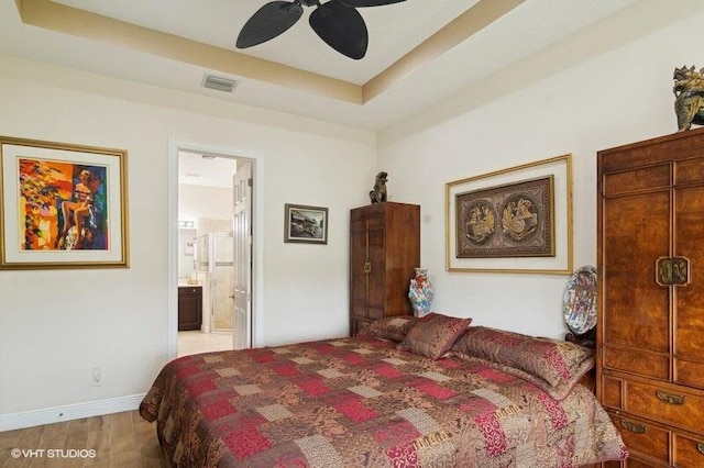 bedroom featuring light wood-type flooring, ceiling fan, connected bathroom, and a raised ceiling