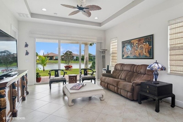 living room featuring ceiling fan, a tray ceiling, a water view, and light tile patterned flooring