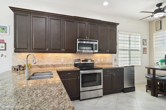 kitchen with stainless steel appliances, backsplash, light stone countertops, dark brown cabinetry, and sink